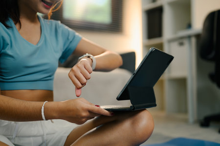 Young woman checking her smartwatch and following an online fitness session at home.の写真素材