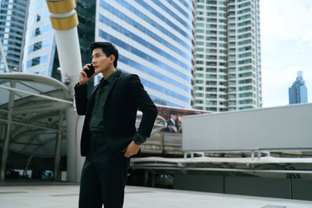 Businessman making a phone call outdoors with modern skyscrapers in the background.の写真素材