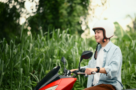 Happy asian man wearing a helmet scooter rider cruising through green countryside.の写真素材