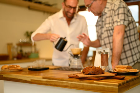 Sliced loaf of bread on a wooden countertop with father and son preparing coffee in background.の写真素材