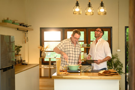 Father and adult son sharing laughter while cooking in a cozy home kitchen. Fathers day concept.の写真素材