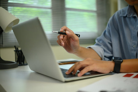 Close up of hands typing on a laptop while working in a modern workspace.の写真素材