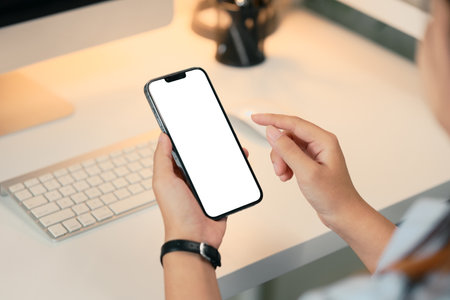 Close up of woman using a smartphone with blank screen at modern desk.の写真素材