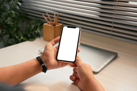 Close up of hands holding a smartphone with blank screen in a modern workspace.の写真素材