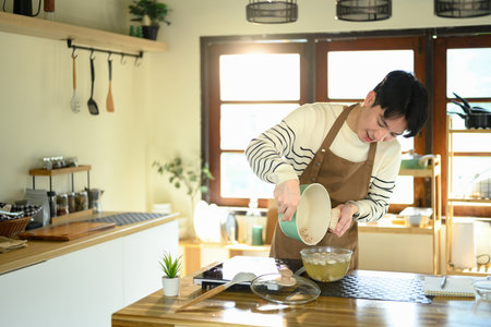 Cheerful man wearing apron finishing up meal prep with care and attention.の写真素材