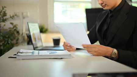 Businessman in formal suit reviewing financial documents at modern office desk.