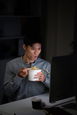 Man eating instant noodles while working late at computer.の写真素材