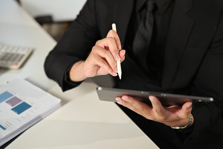 Close up of businessman in black suit using digital tablet with stylus pen.の写真素材
