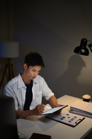 Businessman analyzing documents and taking notes on digital tablet at office desk.の写真素材