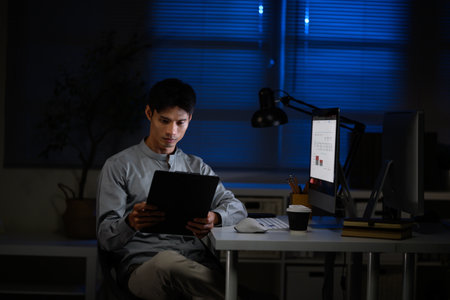 Office worker analyzing business report, working late hours with desktop computer on desk.の写真素材