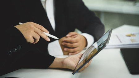Colleagues analyzing financial data and workflow charts with digital tablet in an office.の写真素材