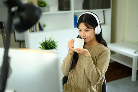 Young woman wearing headphones enjoying a cup of coffee while working at home.