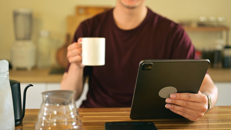 Close up of a man holding a coffee mug while using digital tablet in the kitchen.の写真素材