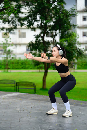 Fit woman wearing headphones practicing bodyweight squats on a stone surface.