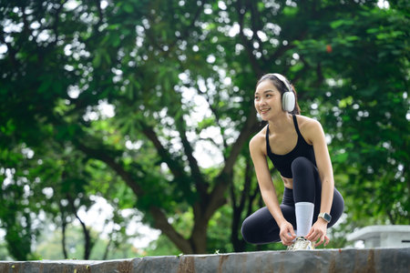 Smiling young woman in sportswear crouching outdoors, tying shoelaces before a workout.の写真素材