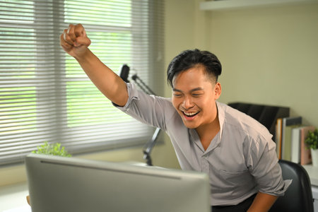 Happy businessman celebrating success in front of computer with excitement in an office.の写真素材