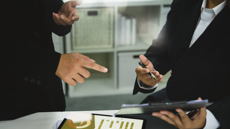 Close up of businesspeople in formal suits discussing charts and reports during office meeting.