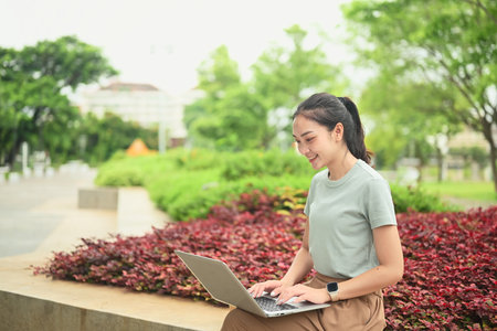 Happy female freelancer using a laptop in a green park, enjoying remote work lifestyle.の写真素材