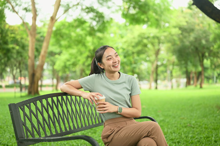 Cheerful woman sitting on a bench in the park, laughing and looking relaxed.の写真素材