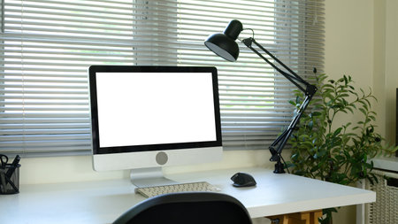 Modern workspace with desktop computer and blank screen on desk near window blinds.