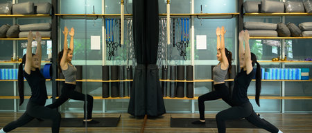 Two women practicing yoga together in a fitness studio, performing a warrior pose.
