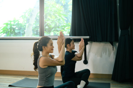 Female yoga students meditating in a fitness studio, focusing on mindfulness, and breathing.