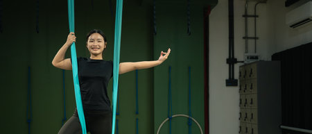 Young woman practicing aerial yoga with hammock fabric, smiling confidently while balancing.