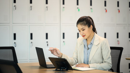Professional businesswoman in beige suit using laptop and tablet in a modern office.