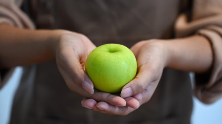 Close up of hands holding a fresh green apple, symbolizing healthy eating and nutrition.の写真素材