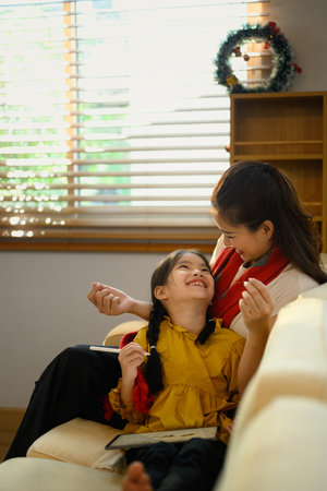 Happy mother and daughter share a joyful moment while sitting on a sofa in a bright living room.の写真素材