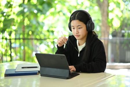 Young student in black hoodie using tablet for study, listening to educational content with headphones.の写真素材