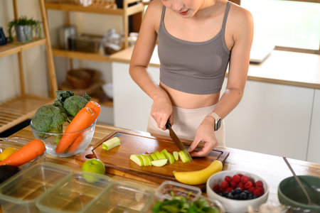 Active woman in sportswear slicing vegetables for weekly meal prep in a modern kitchen.の写真素材