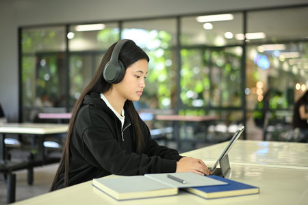 High school student studying with headphones, using digital tablet in quiet study area.