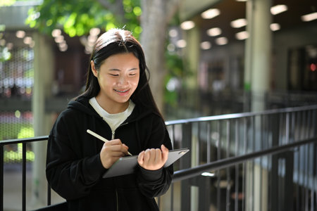 Teen girl using a digital tablet with stylus in an open school environment.の写真素材
