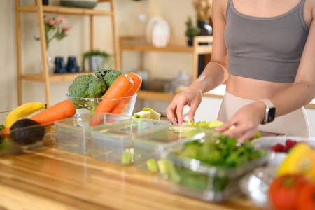 Fitness woman packing nutritious ingredients or weekly meal prep in a bright kitchen.の写真素材