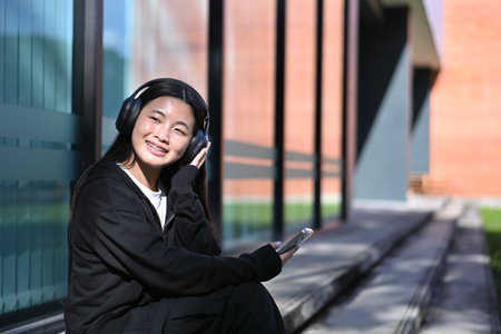 Teen girl wearing black hoodie and wireless headphones, enjoying her favorite songs outside a modern...
