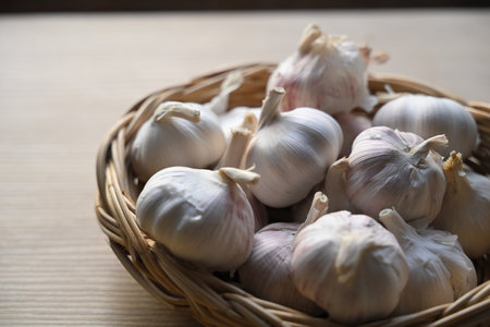 Close up of fresh garlic bulbs placed in a woven basket, natural light highlighting texture and...