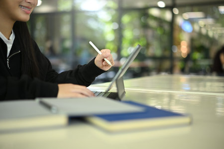 Close-up view of young female student working on digital tablet for homework or virtual class.