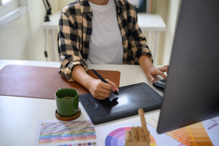 Creative artist using pen tablet and computer for digital illustration or logo design in a cozy...