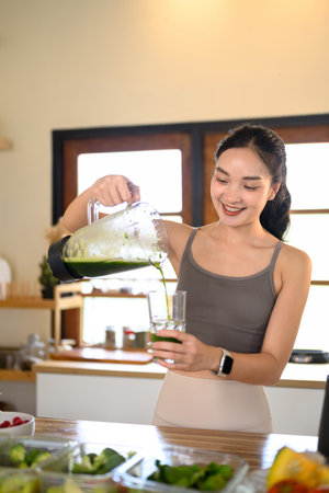 Young woman in activewear preparing a fresh vegetable smoothie for a balanced diet.の写真素材