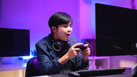 A young man enjoying playing computer games in a neon-lit room. The gaming atmosphere features vibrant colors.の写真素材
