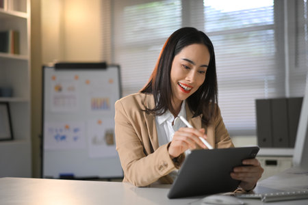 Confident businesswoman working on digital tablet in office, representing modern career, technology, and professional lifestyle.の写真素材