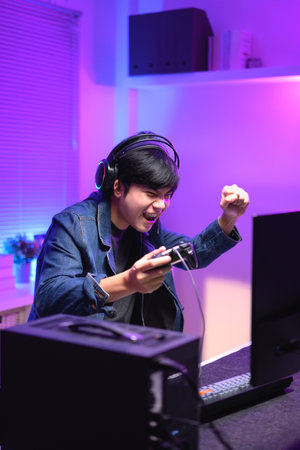 A young man enjoying playing computer games in a neon-lit room. The gaming atmosphere features vibrant colors.の写真素材