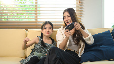 Mother teaching her daughter how to play a video game, sharing laughter and learning through fun...