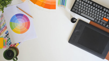 Top view of creative workspace with color palette, digital tablet, and notebook sketching logo design on clean white desk.の写真素材