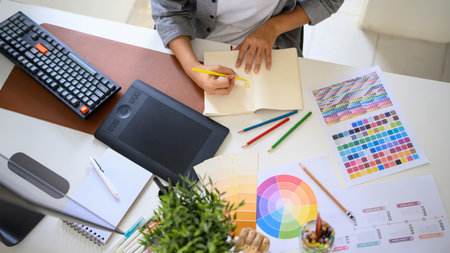 Top view creative woman sketching logo ideas in notebook with color samples and pencils.の写真素材