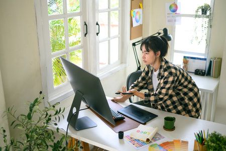 Creative editor reviewing and checking design details on computer with digital pen and color chart in modern workspace.の写真素材