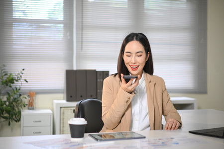 Smiling businesswoman talking on smartphone using speakerphone in office, expressing positivity.の写真素材