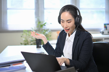 Smiling businesswoman wearing headset talking during online meeting, representing customer service...