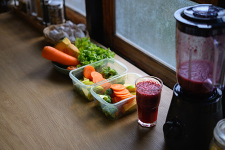 Fresh vegetables, fruits, and a red smoothie on a wooden table in a cozy kitchen, representing clean...